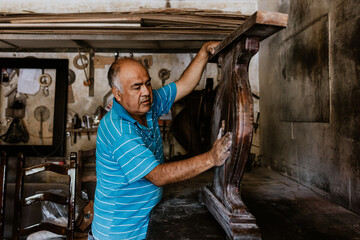 hispanic senior man carpenter using sandpaper on a polished wood in workshop in Mexico Latin America
