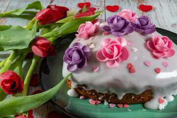 Heart-shaped cake with lemon icing decorated with pink and purple flowers.