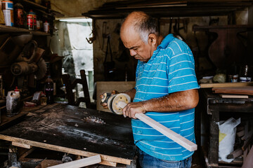 hispanic senior man carpenter using sandpaper on a polished wood in workshop in Mexico Latin America
