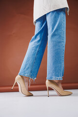 Close-up of female legs in blue jeans and fancy beige high heels. Women's leather pumps.