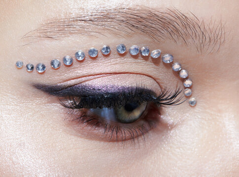 Closeup macro shot of human female eye with unusual makeup. Woman with rhinestones arrows on eyelid. - Powered by Adobe