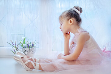 Little girl ballerina. Ballerina in a tutu. The girl is sitting at the window. Thoughtful girl ballerina. Little beautiful girl. Girl in pointe shoes.