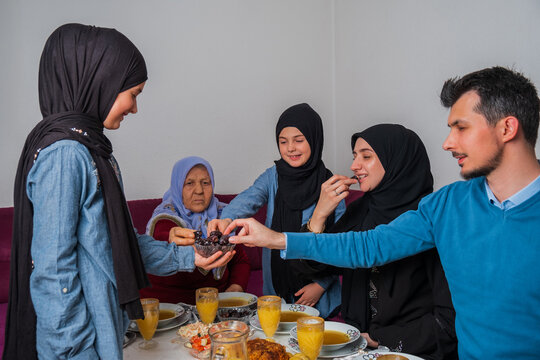 Happy Muslim family having iftar dinner at home during Ramadan dining table eating dates to break fast.