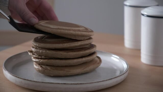 Woman cooking pancakes and stacking them on a plate.