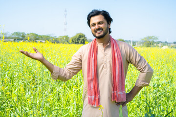 Portrait shot of happy smiling famer showing farmland by loooking at camera - concept of happiness,...