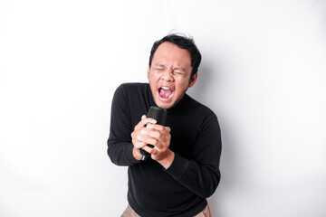 Portrait of carefree Asian man, having fun karaoke, singing in microphone while standing over white background