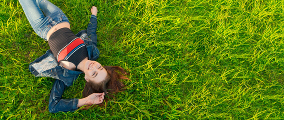 Young Woman lying in nature on green grass in park, relaxing smiling, her red hair flying in the...