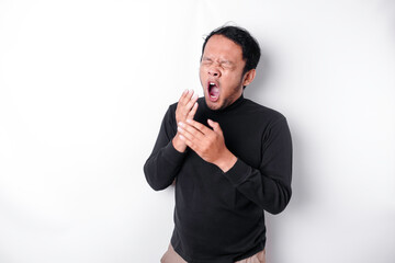 Portrait of sleepy attractive Asian man wearing a black shirt, feeling tired after night without sleep, yawning, covering opened mouth with palm
