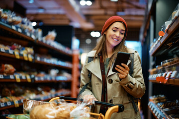 Happy woman using app on smart phone while shopping groceries in supermarket.