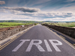 Small narrow high quality asphalt road with stone fences on each side and big sign trip. Blue cloudy sky and green fields. Warm sunny day. West of Ireland. Tourism concept.