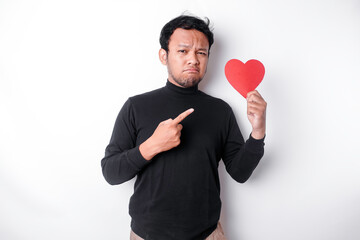 A portrait of an Asian man wearing a black shirt looks so confused while holding a red heart-shaped...