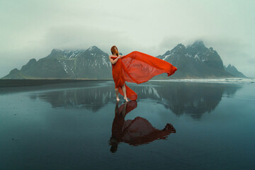 Sensual woman in red clothes on Reynisfjara beach scenic photography. Picture of person with hills on background. High quality wallpaper. Photo concept for ads, travel blog, magazine, article