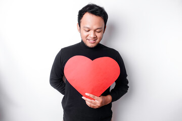 Obraz na płótnie Canvas A portrait of a happy Asian man wearing a black shirt, holding a red heart-shaped paper isolated by white background