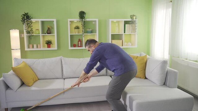 Mature man mopping floor with mop in living room at home and getting tired.
Mature man wiping floor with mop during house cleaning. Tired and sluggish mature man.

