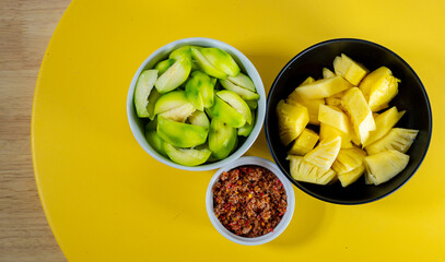 A pile of fresh Elaeocarpus hygrophilus and pineapple fruits. Cut it in half and put it in a cup. on a yellow background
