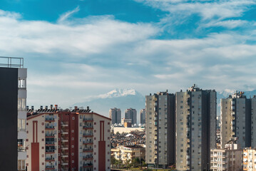 Obraz premium Snowy mountain peak visible through city buildings on a sunny day