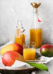 Glass of homemade of delicious mango juice and glass bottles with fresh ripe fruit and leaves. Homemade organic food concept. Copy space. Selective focus.