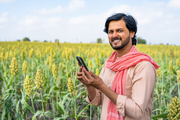 Farmer with mobile phone at agricultural farm land looking at camera showing with copy space - concept of technology, banking or financial and modern village farmer
