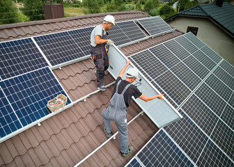 Men workers mounting photovoltaic solar moduls on roof of house. Engineers in helmet installing solar panel system outdoors. Concept of alternative and renewable energy. Aerial view. © anatoliy_gleb