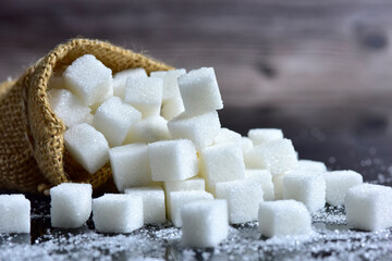 Closeup White sugar cubes and refined sugar in burlap sack bag on a black background. selective focus.