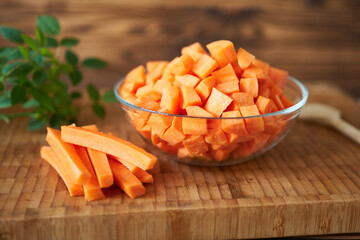 Dice carrots in a glass bowl and slice on a wooden board. Rustic style.