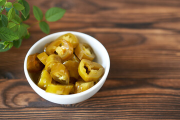 Canned pickled jalapeño peppers in a bowl on a wooden background. Rustic style.