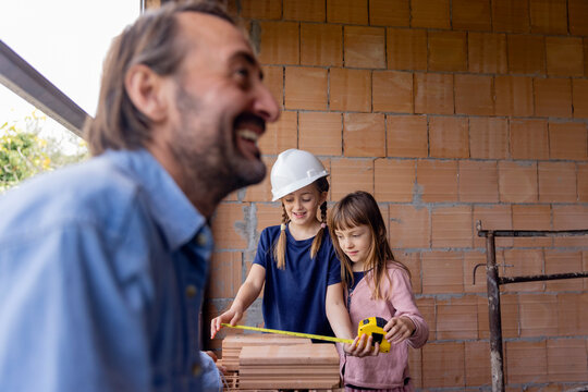 Happy man with daughters measuring bricks in front of wall