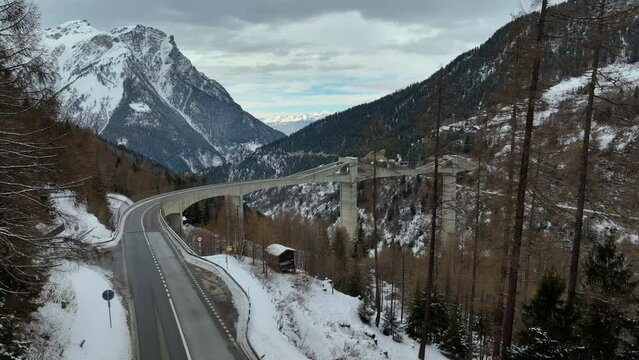 Wide drone shot of the ultra modern Ganter Bridge between the high swiss peaks of the  alps covered during wintertime. 