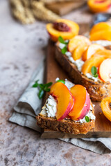 Open sandwiches with tartine bread and cream cheese, nectarine and apricot drizzled with honey on wooden cutting board. Concrete background.