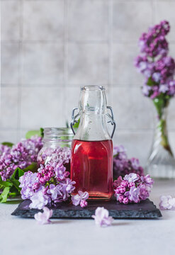 Preparation of syrup from the lilac flowers. Glass jar of homemade lilac syrup and branch of lilac flowers, stone background.