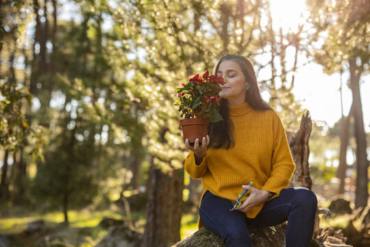 Mature woman sitting on a rock smelling at potted flower
