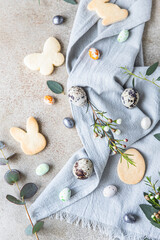 Fototapeta na wymiar Easter cookies with candies shaped eggs, floral decor and quail eggs on linen napkin on stone background. Holiday concept.
