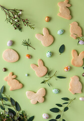 Easter cookies, candies shaped eggs, eucalyptus, flowers and quail eggs, green pastel background. Happy Easter concept. Pattern.