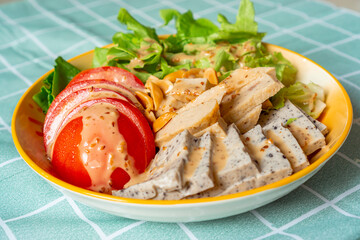 Sesame tofu with salad and sliced tomato on dish with roast sesame salad cream