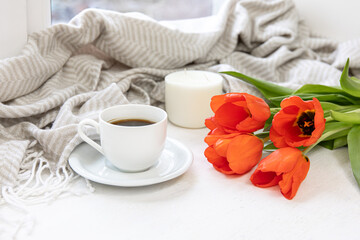 Home composition with a cup of coffee, red tulips and a candle.