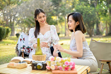 Two beautiful Asian women in lovely dresses enjoying afternoon picnic in the park