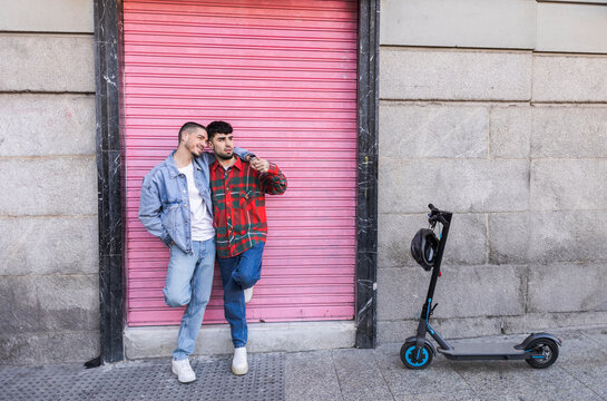 Happy gay couple standing in front of roller shutter by electric push scooter