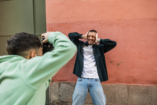 Man clicking photos of friend gesturing in front of wall