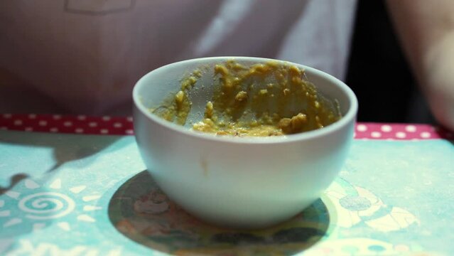 Eating some vegetable mush from a bowl with a spoon