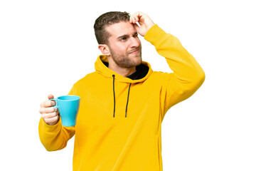 Young handsome blonde man holding cup of coffee over isolated background having doubts and with...