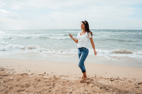 Woman using smart phone walking on sand at beach