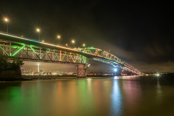 Fototapeta na wymiar Auckland Harbour Bridge glowing in green, blue and orange. Auckland, New Zealand