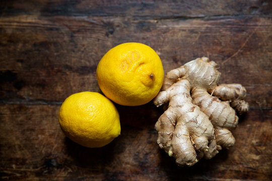 Two fresh lemons and ginger root lying on wooden surface