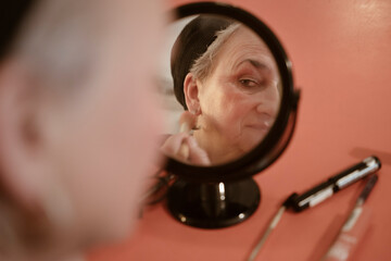Senior woman looking in mirror doing make up at home