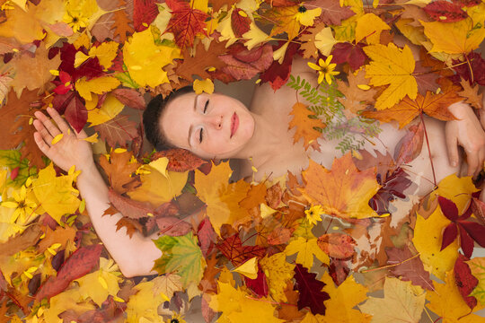 Woman relaxing with autumn leaves in bathtub