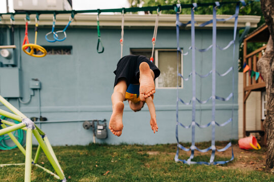 Caucasian boy swings upside down joyfully on play set in backyard