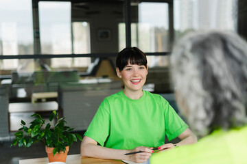 Smiling woman in green t-shirt looking at colleague in office