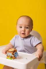 a cute kid is sitting in a child's chair playing with an educational wooden toy on a yellow background. bizi-board