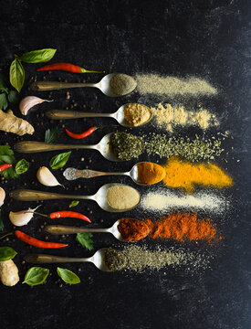 Overhead of spoons full of herbs and spices on a black background.