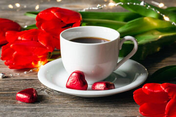 Composition with a cup of coffee, heart-shaped sweets and red flowers close-up.